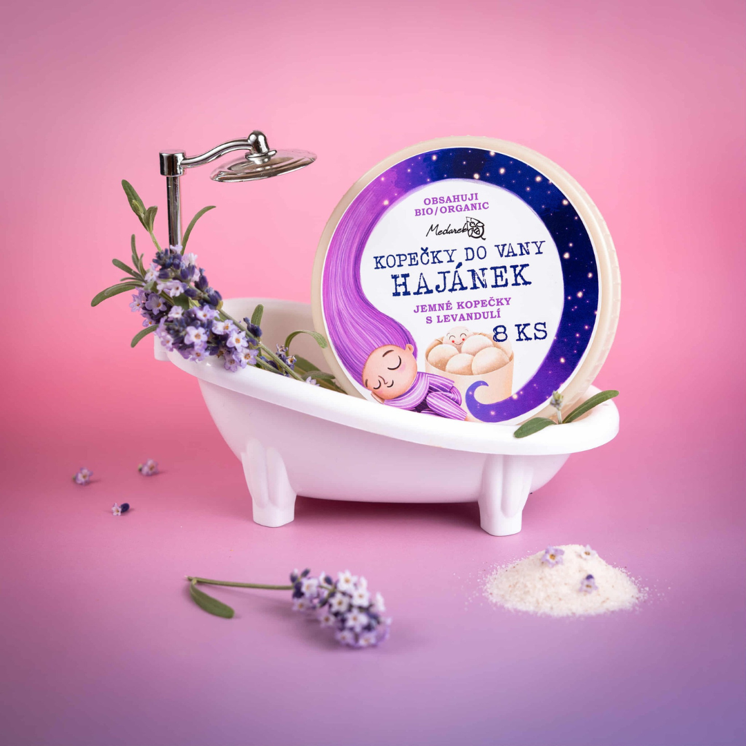 lavender-themed product photo of “Kopečky do vany Hajánek” bath melts in a small white toy bathtub with sprigs of lavender on a pink background